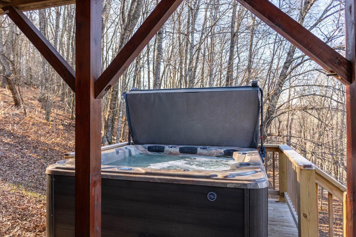 A hot tub sits invitingly on the deck, surrounded by lush trees and wooden decking. The setup conveys an atmosphere of relaxation and luxury, perfect for unwinding after outdoor adventures.