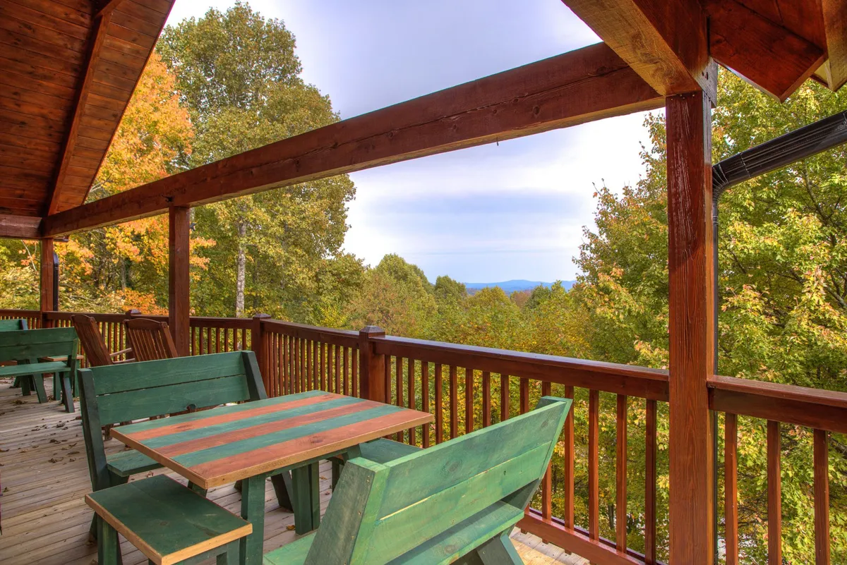 The expansive wrap-around wooden deck furnished with tables and chairs, surrounded by lush greenery and offering spectacular mountain views. The deck is ideal for outdoor dining, morning coffee, or simply soaking in the scenery.