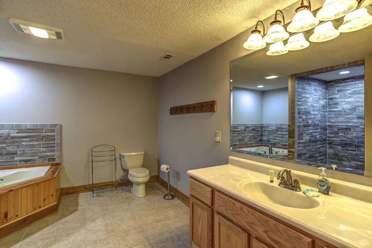 A tranquil, inviting bathroom featuring a spacious bathtub, a sink with a broad mirror, and a toilet. The soft lighting and clean design evoke a spa-like atmosphere, perfect for unwinding after energetic play in the family room.