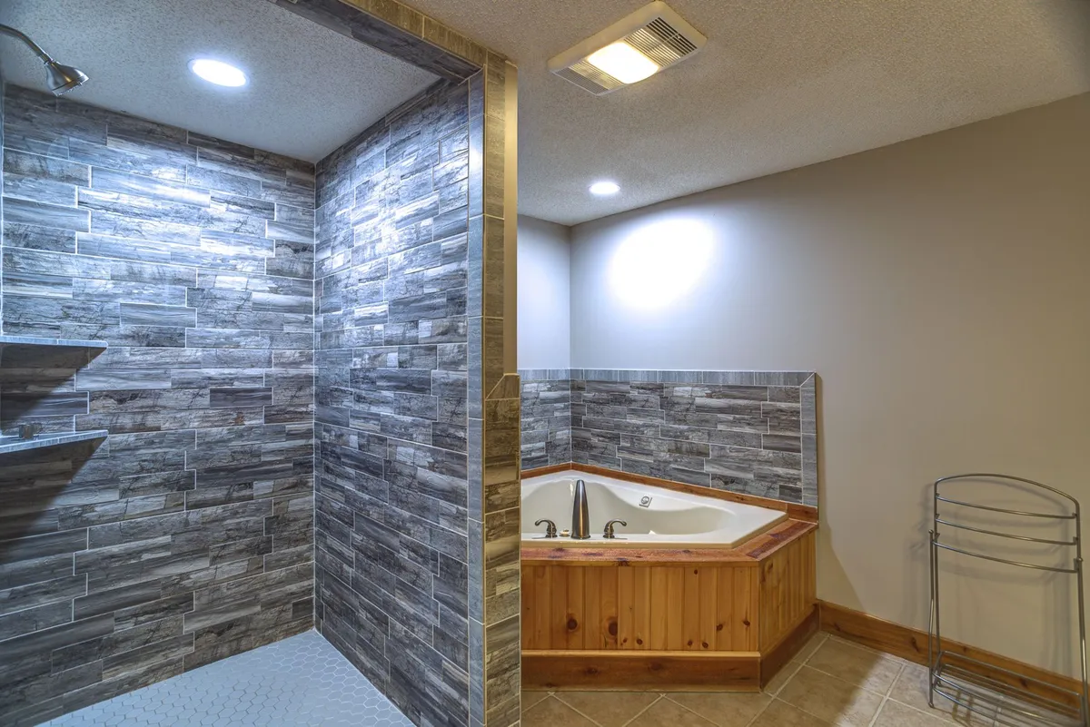 A serene bathroom scene showcasing a jacuzzi tub and a separate shower area with textured wall tiles, suggesting ample space and options for bathing and relaxation. The ambiance is calm and spa-like.