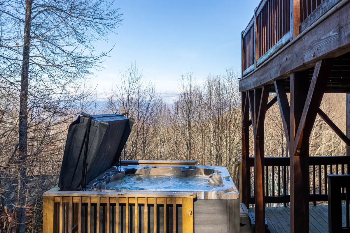 A serene hot tub placed on a wooden deck, surrounded by trees and open sky, inviting guests to relax while enjoying the peaceful mountain atmosphere. The setup suggests both daytime relaxation and evening stargazing.
