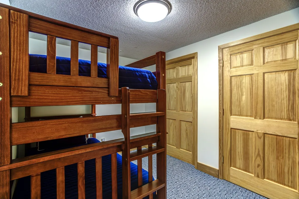 A compact, cozy alcove featuring a bunk bed, soft carpeting, and wooden doors. The playful arrangement makes it an ideal nook for kids' naps, sleepovers, or a separate space for teens.