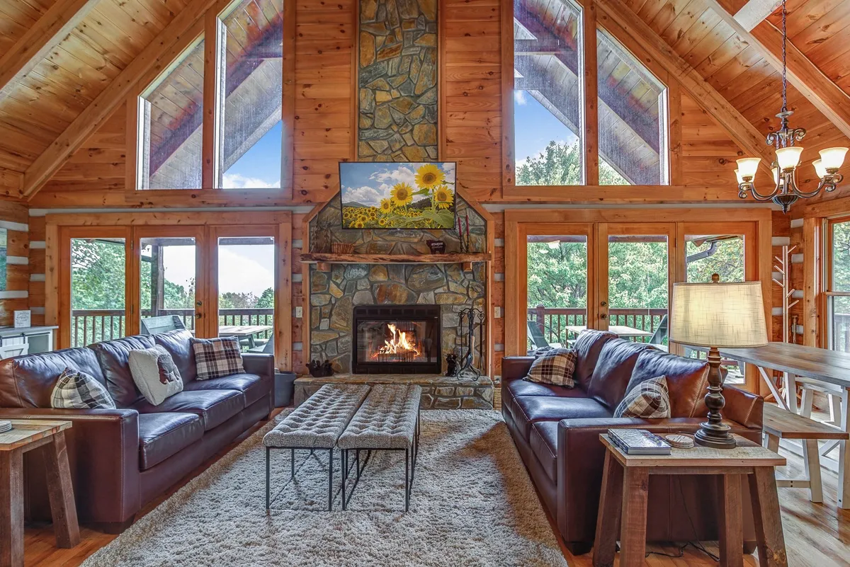 This interior image centers on a cozy fireplace flanked by large windows, leather sofas, and a coffee table, all set in a warm and welcoming living area. The windows frame views of the outdoors, inviting natural light and scenic beauty into the space.
