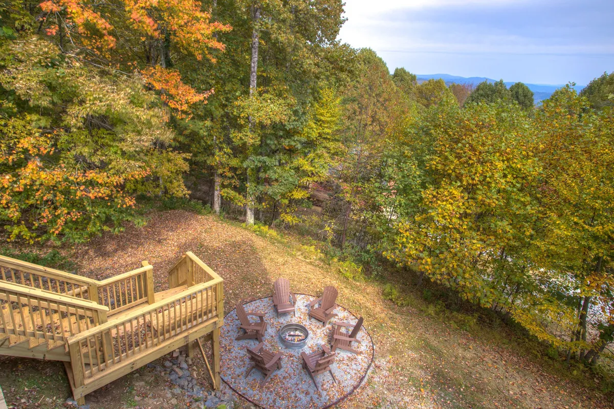 The image focuses on a deck area with a cozy fire pit, surrounded by Adirondack chairs and trees. The space invites gatherings for marshmallow roasting, storytelling, and stargazing under the open sky.